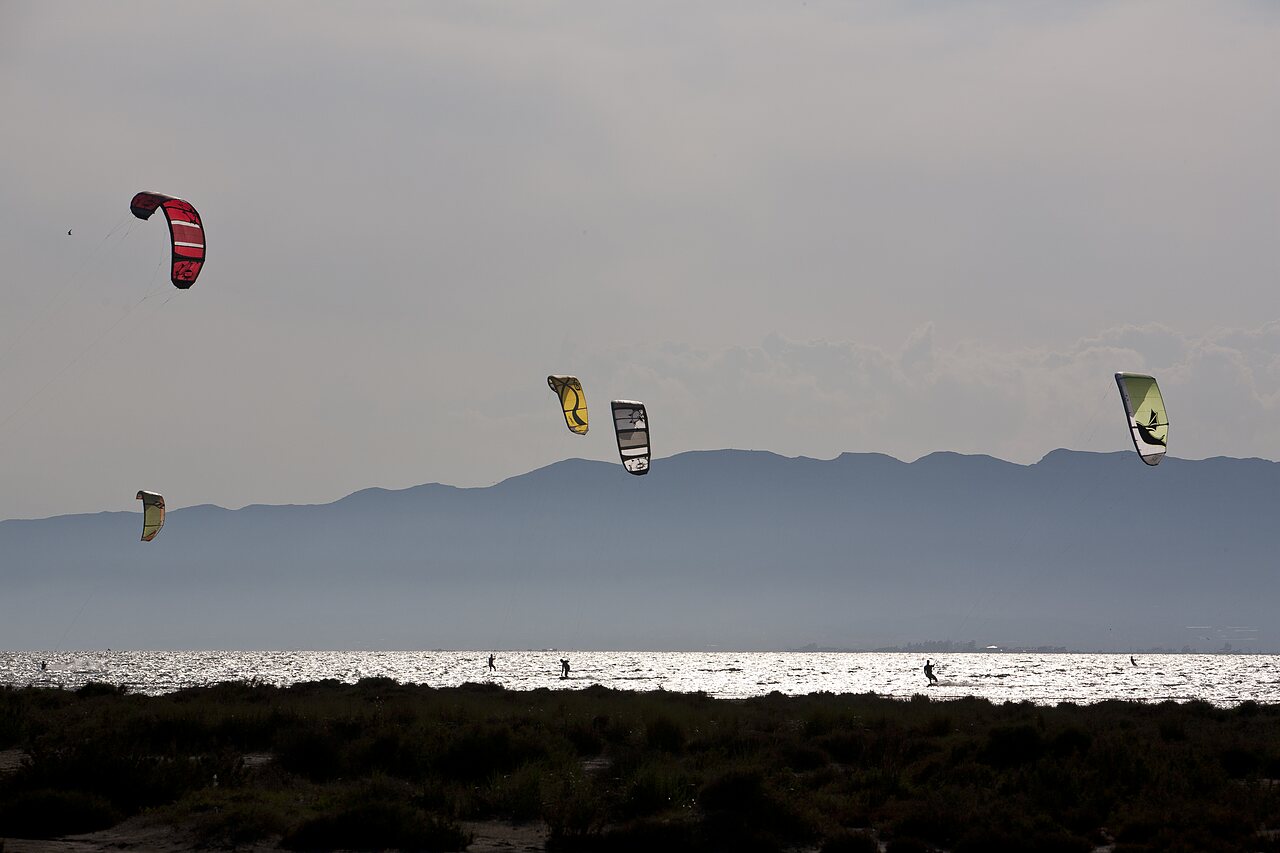 Kitesurfers sur l'eau scintillante avec montagnes au camping CAPFUN Aube � Deltebre, Tarragone.