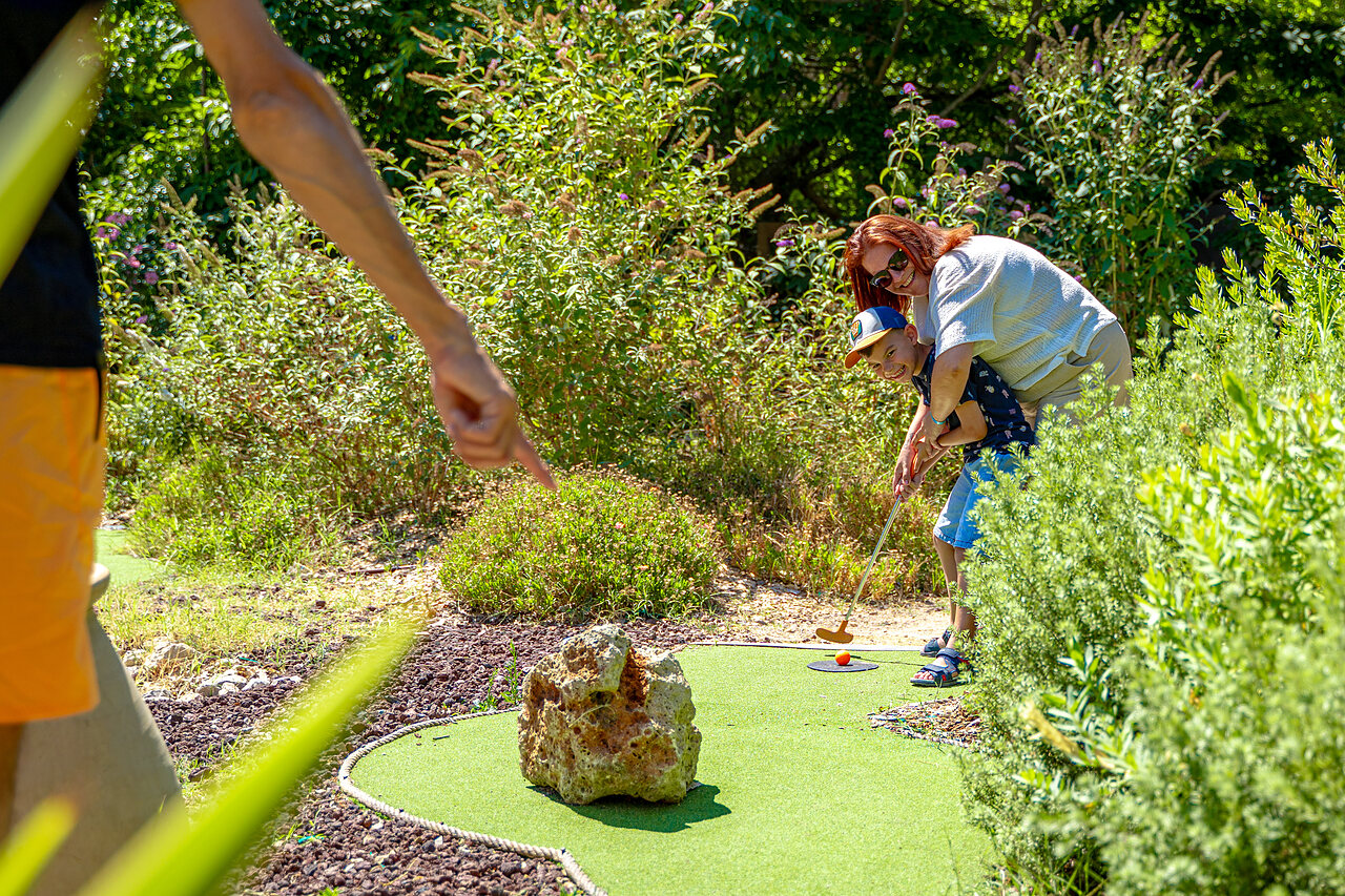Enfant et adulte jouant au mini-golf sur un parcours verdoyant au camping CAPFUN Aubr�des � Puget sur Argens (83).