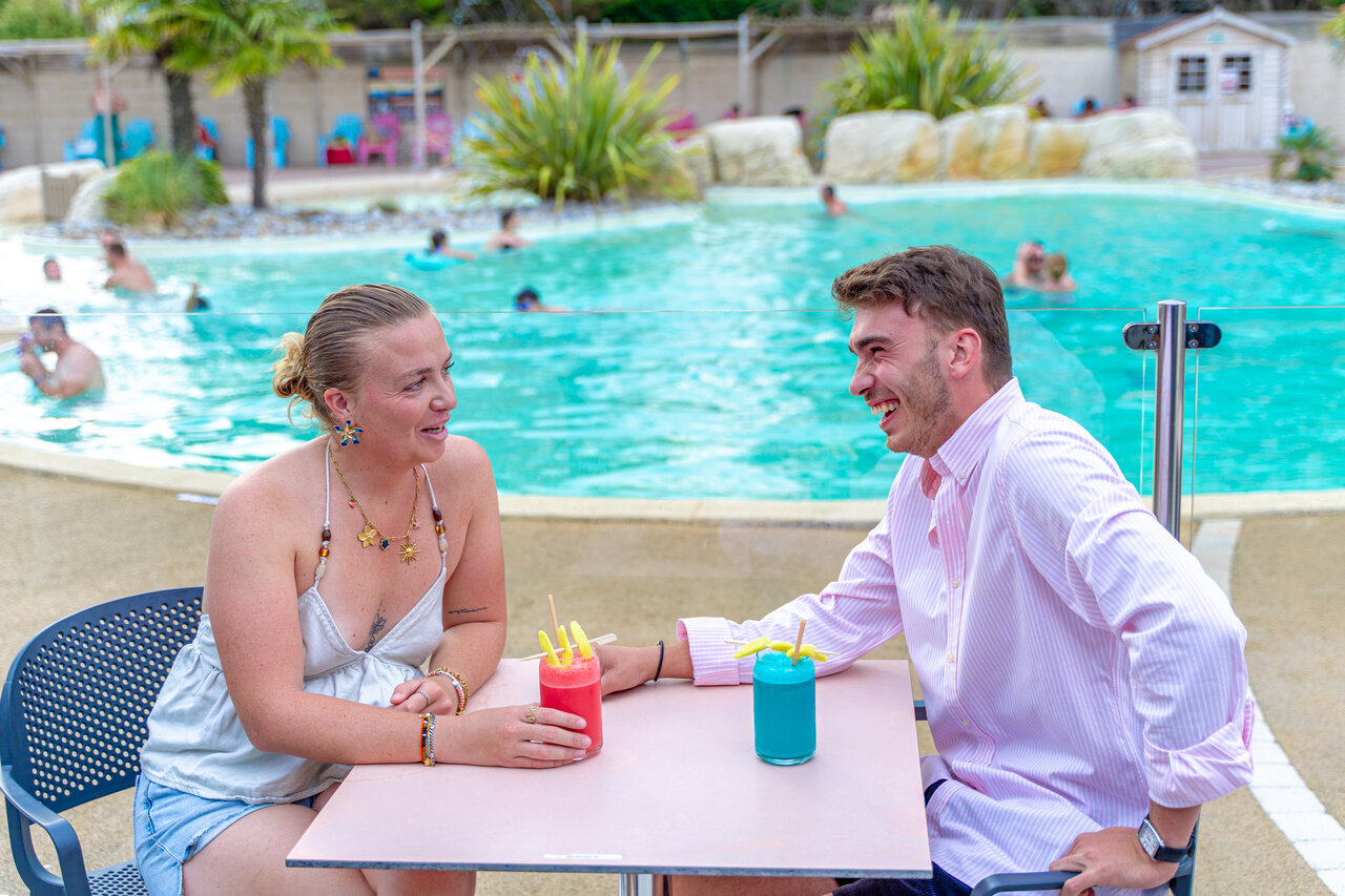Couple souriant d�gustant cocktails pr�s de la piscine au camping VAGUES OCEANES Bois Joly � Saint-Jean-de-Monts (85).