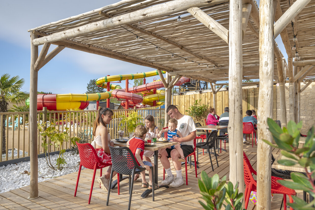 Famille d�jeunant sur la terrasse du restaurant avec toboggans aquatiques au camping CAPFUN Chateau d'Arvid � Villerville (14).
