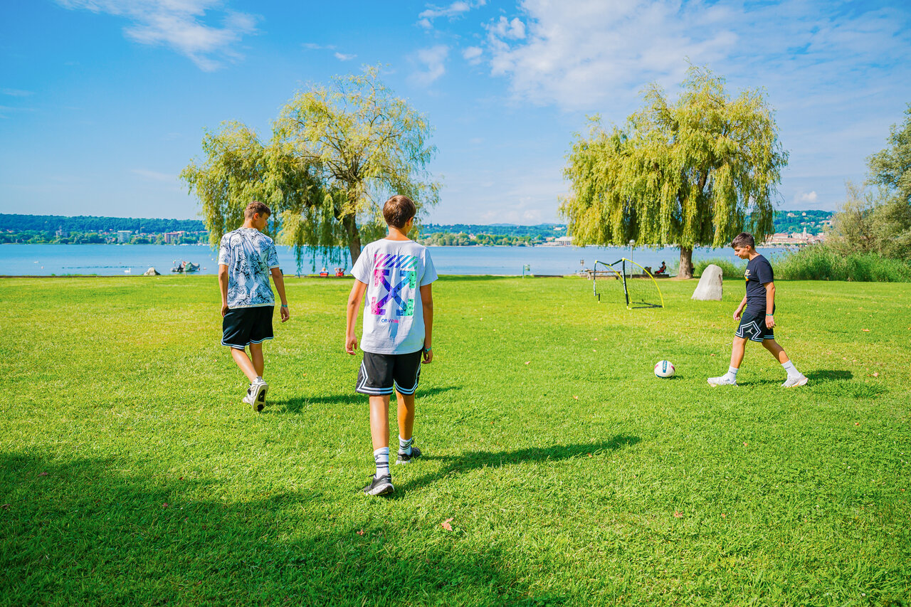 Gar�ons jouant football sur pelouse, lac, au camping CAPFUN Citta di Angera � Angera VA.