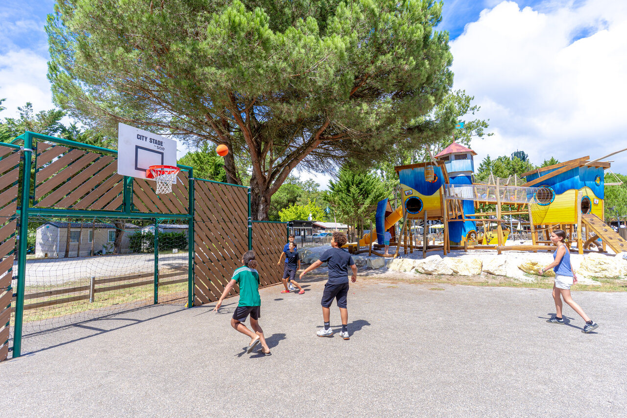 Terrain multisport avec enfants jouant au basket et grande aire de jeux au camping VAGUES OCEANES Coq Hardi � Cassy-Lanton (33).