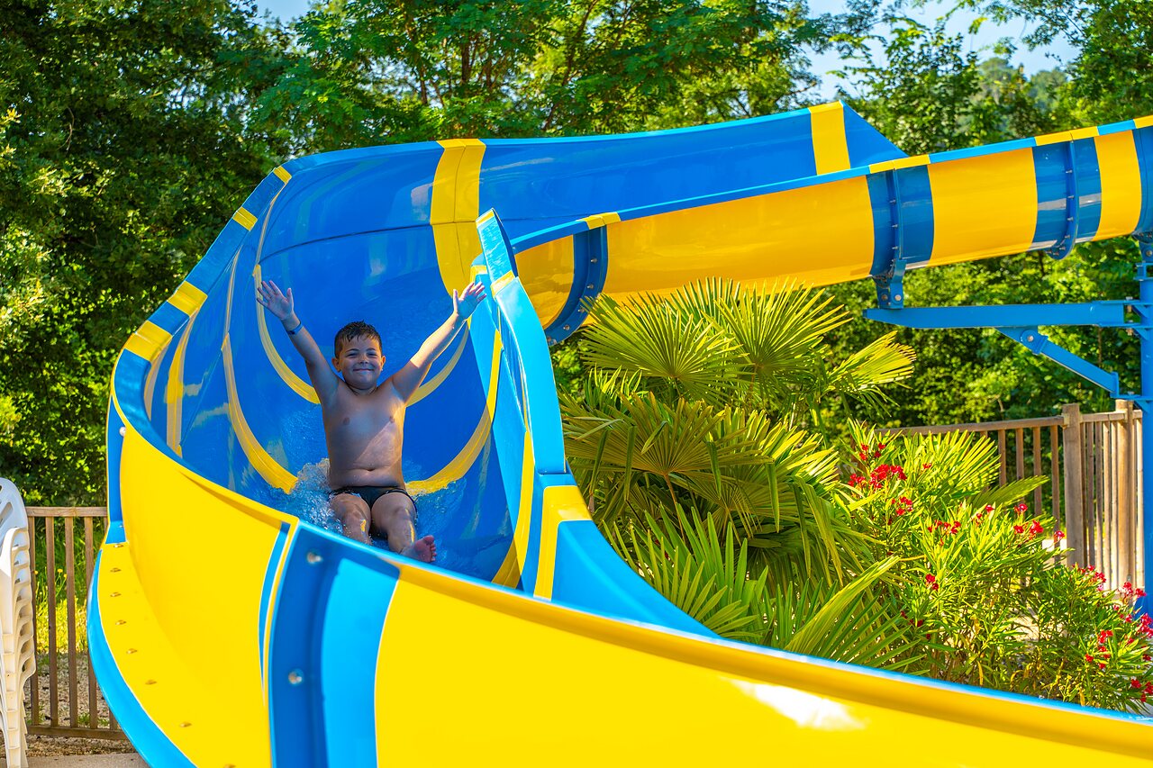 Enfant heureux sur toboggan aquatique bleu et jaune au camping CAPFUN Duravel � Duravel.