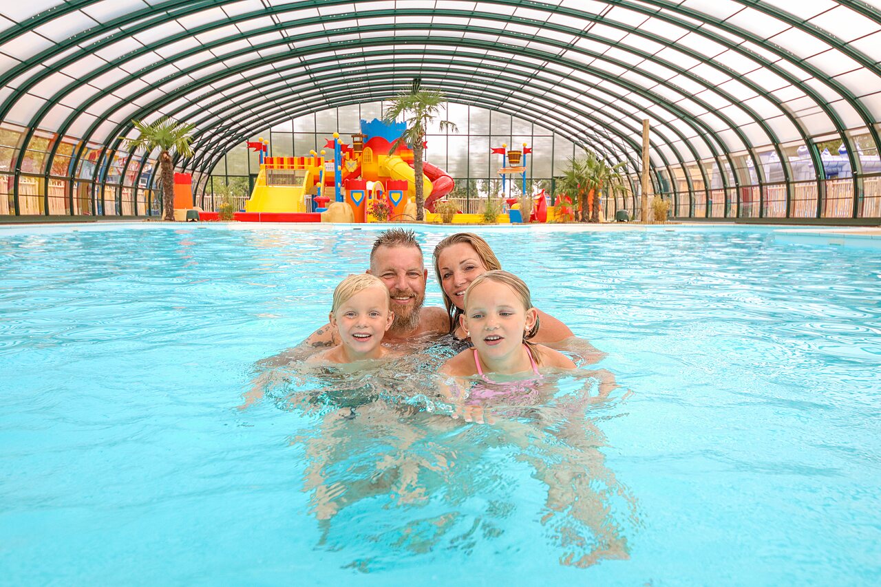 Famille souriante dans la piscine couverte avec jeux aquatiques au CAPFUN Eibernest.