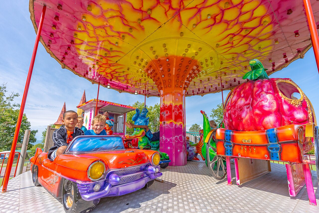 Enfants souriants sur man�ge color� avec voiture au camping CAPFUN Falaises � Gonneville sur Mer.