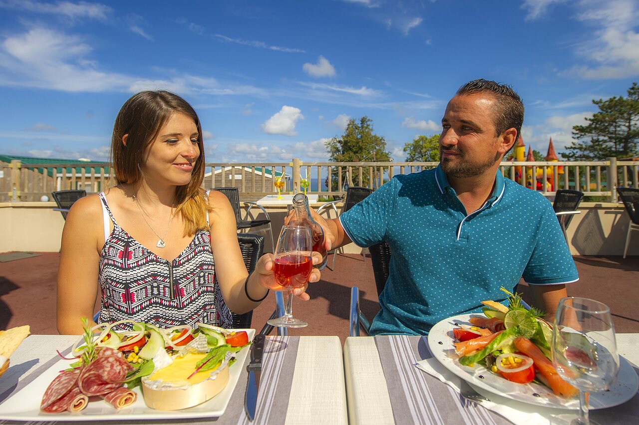 Couple d�nant au restaurant en terrasse, toastant vin ros�, au camping CAPFUN Falaises.