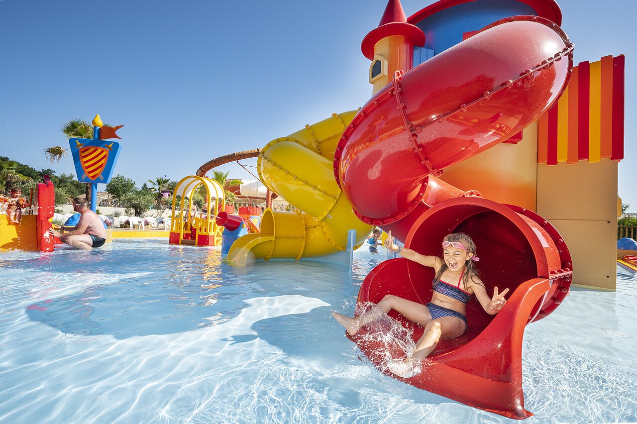 Fille souriante descendant un toboggan aquatique rouge dans la piscine au camping CAPFUN Forges � Avrille (85).