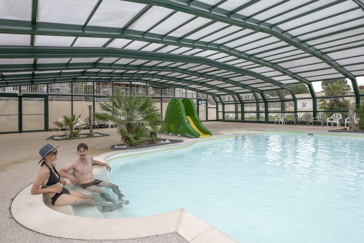 Piscine couverte avec toboggan crocodile et couple au camping CLICOCHIC Haras de Deauville � Touques (14).