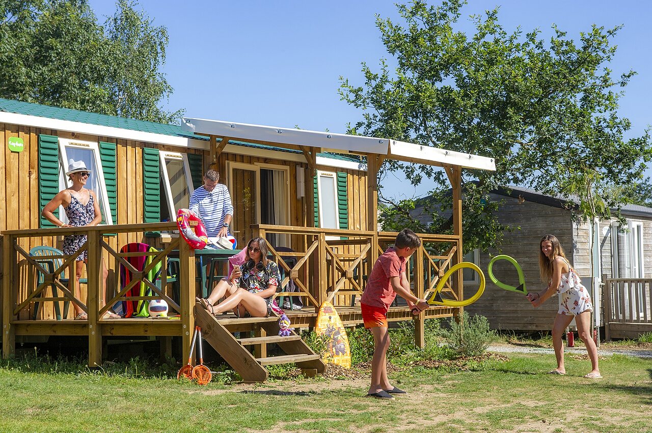 Famille jouant devant un mobile-home avec terrasse au camping CAPFUN Heino � Heino.