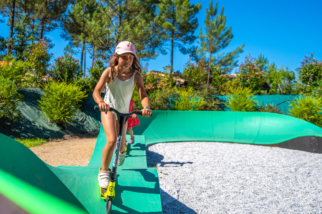 Enfant en trottinette sur pumptrack verte au camping CAPFUN Huttes � Saint-Denis d'Ol�ron.