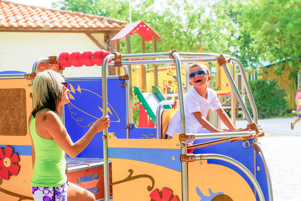 Aire de jeux color�e, enfant et femme souriants, camping CAPFUN Huttes, Saint-Denis d'Ol�ron.