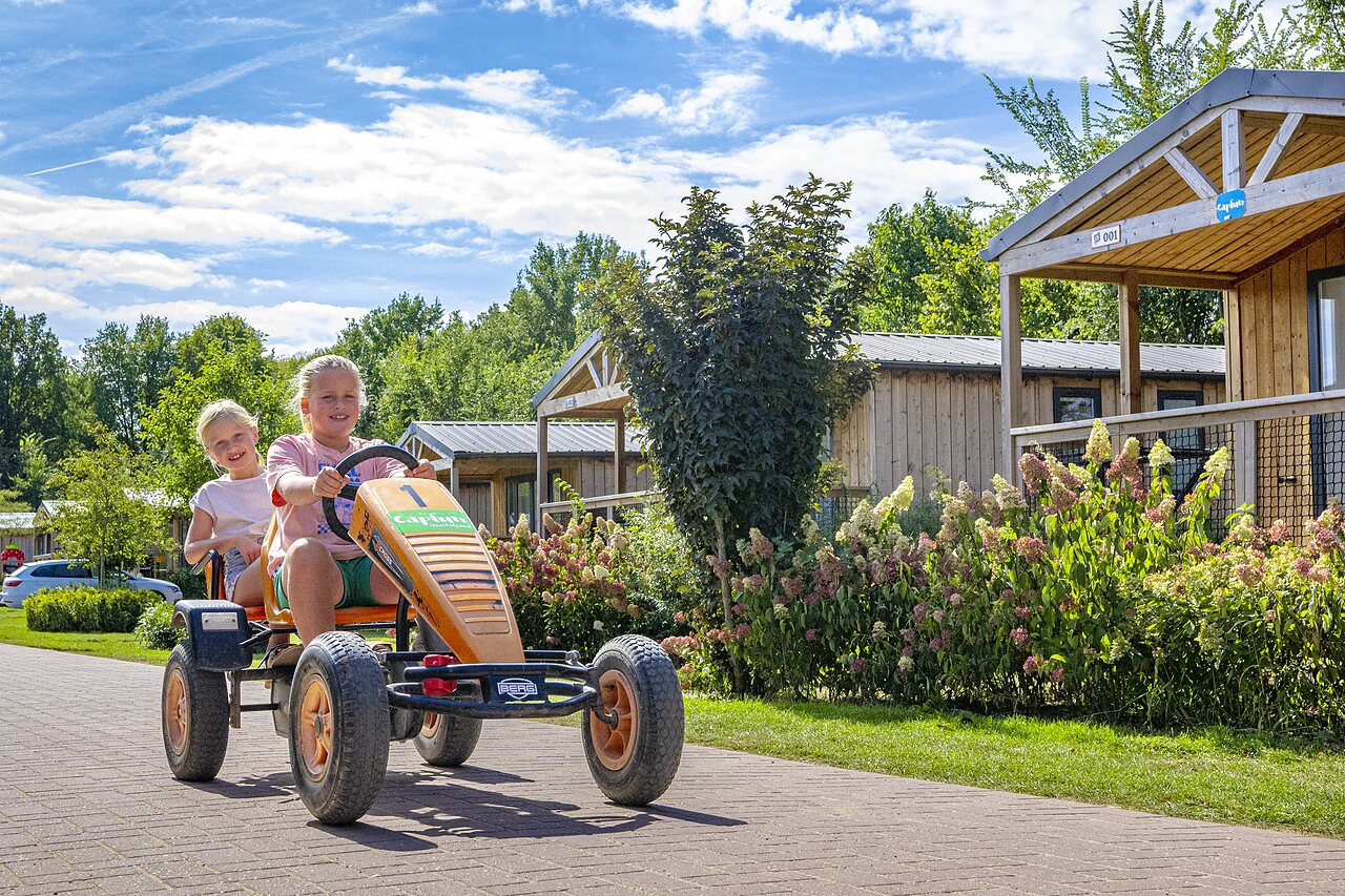 Enfants souriants sur kart � p�dales devant chalets au camping CAPFUN IJsselstrand � Doesburg.