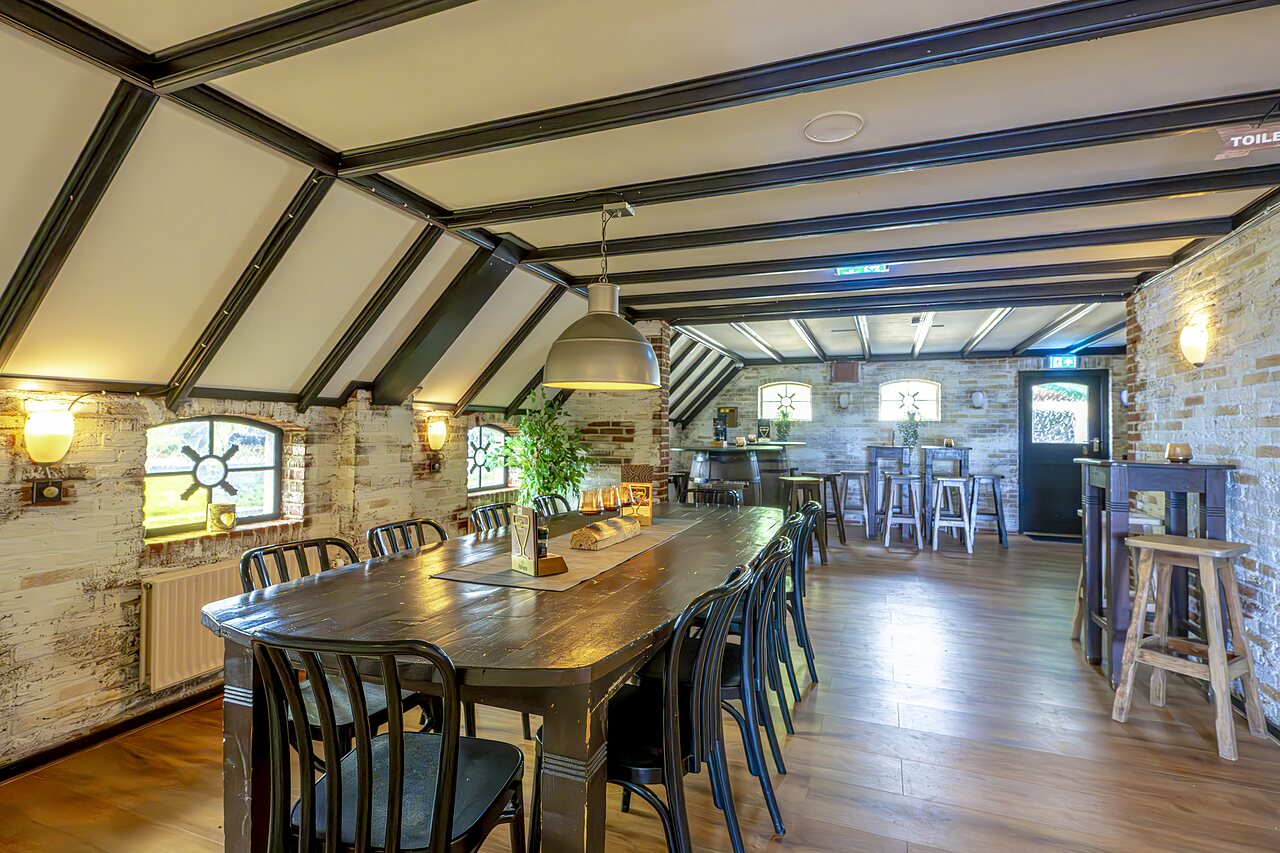 Salle de restaurant avec longue table en bois et bar au camping CAPFUN IJsselstrand � Doesburg.