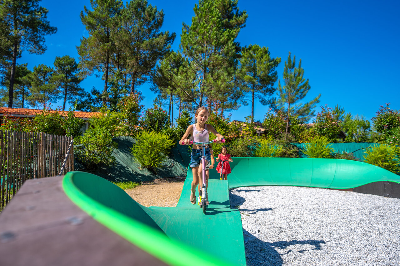Enfants jouant sur un pumptrack vert avec trottinettes au camping CAPFUN Lila � LINXE (40).