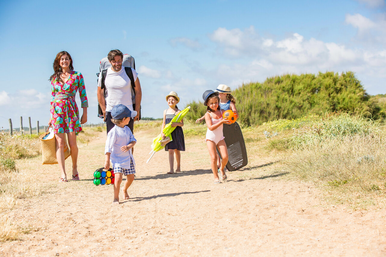 Famille marchant sur un sentier de sable avec �quipements de plage au camping CAPFUN Loubine � Les Sables d'Olonne (85).