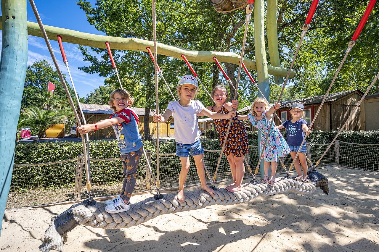 Enfants souriants jouant sur un pont de cordes � l'aire de jeux au camping CAPFUN Lou Puntaou � LEON (40).