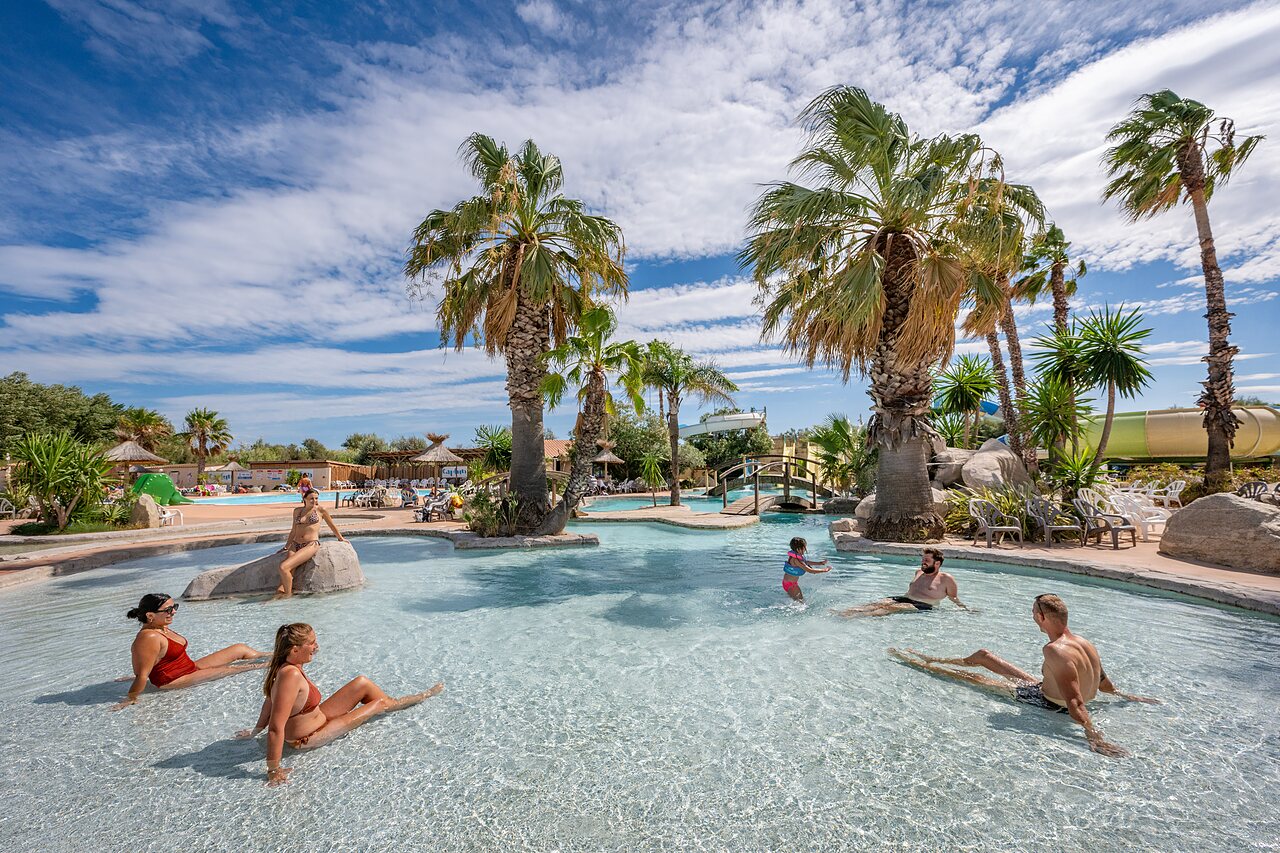 Grande piscine tropicale avec toboggan et palmiers au camping CAPFUN Lou Village � Vendres (34).