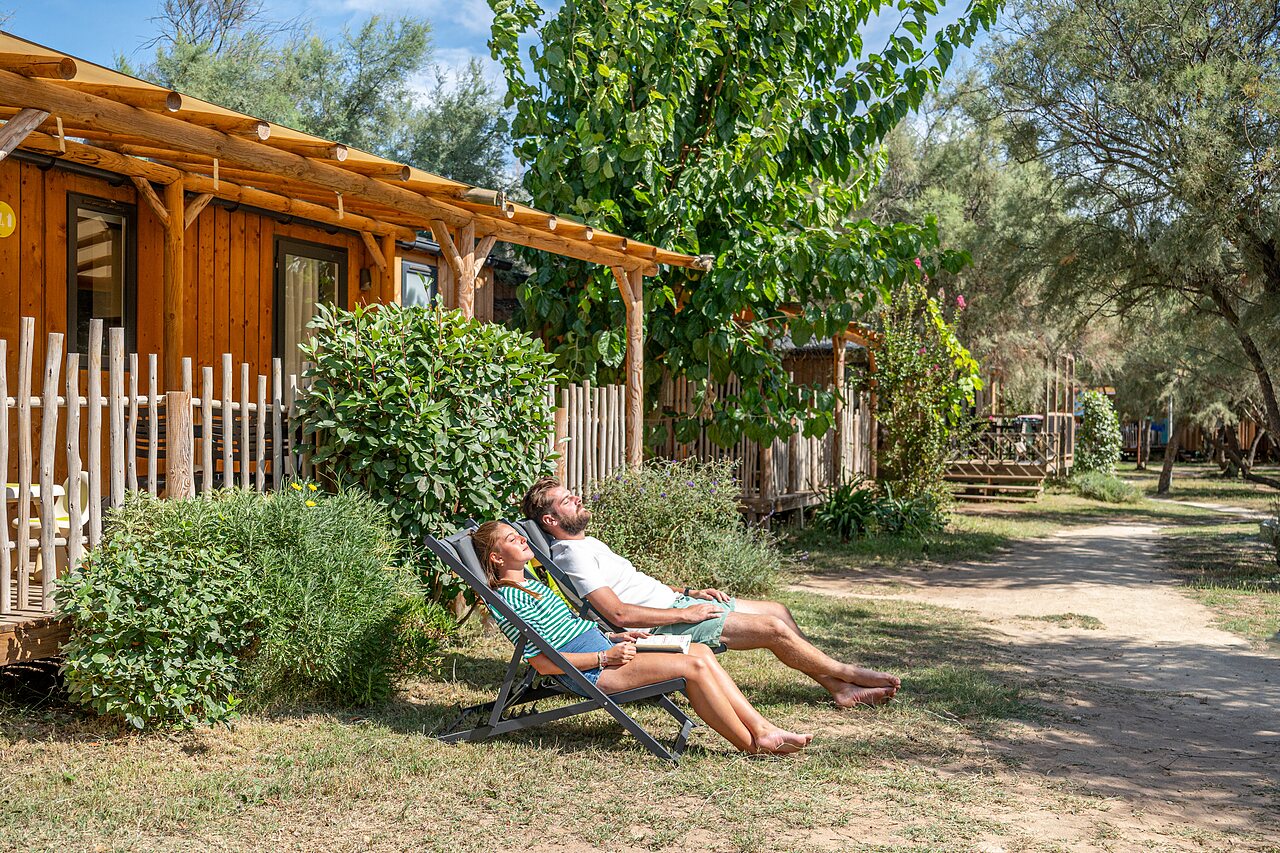 Couple relaxant sur transats devant Mobil-home en bois au camping CAPFUN Lou Village.