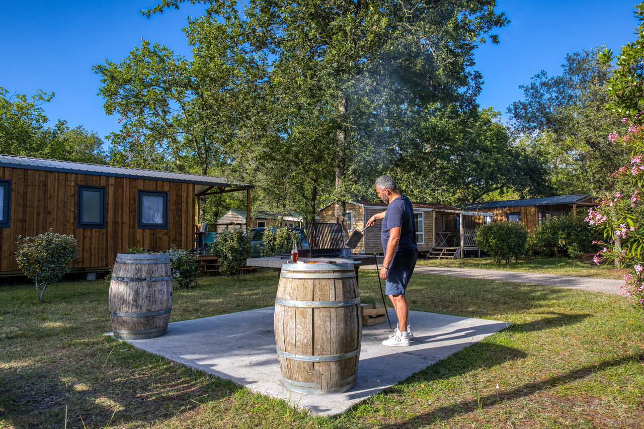 Homme faisant un barbecue devant des Mobil-homes au camping CLICOCHIC M�doc Bleu � Carcans (33).