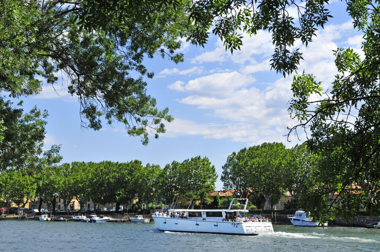 Bateau de promenade sur la rivi�re, bord�e d'arbres verdoyants, au camping CAPFUN Mer et Soleil � Cap d'Agde (34).