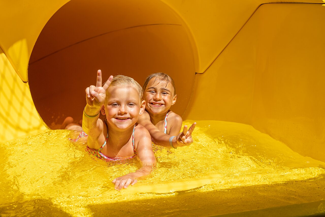 Deux enfants souriants sur un toboggan aquatique jaune au camping CAPFUN Mirabelle � VOLSTROFF (57).