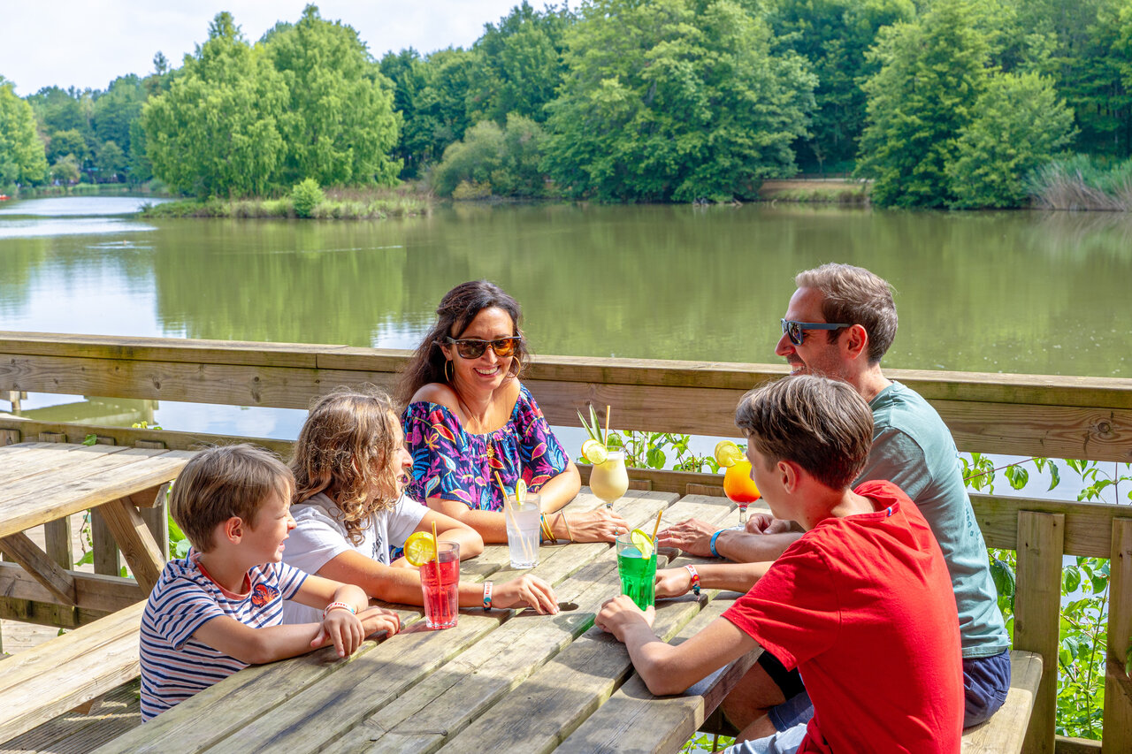Famille souriante buvant cocktails au bar avec vue lac au camping CAPFUN Moulinal � BIRON (24).