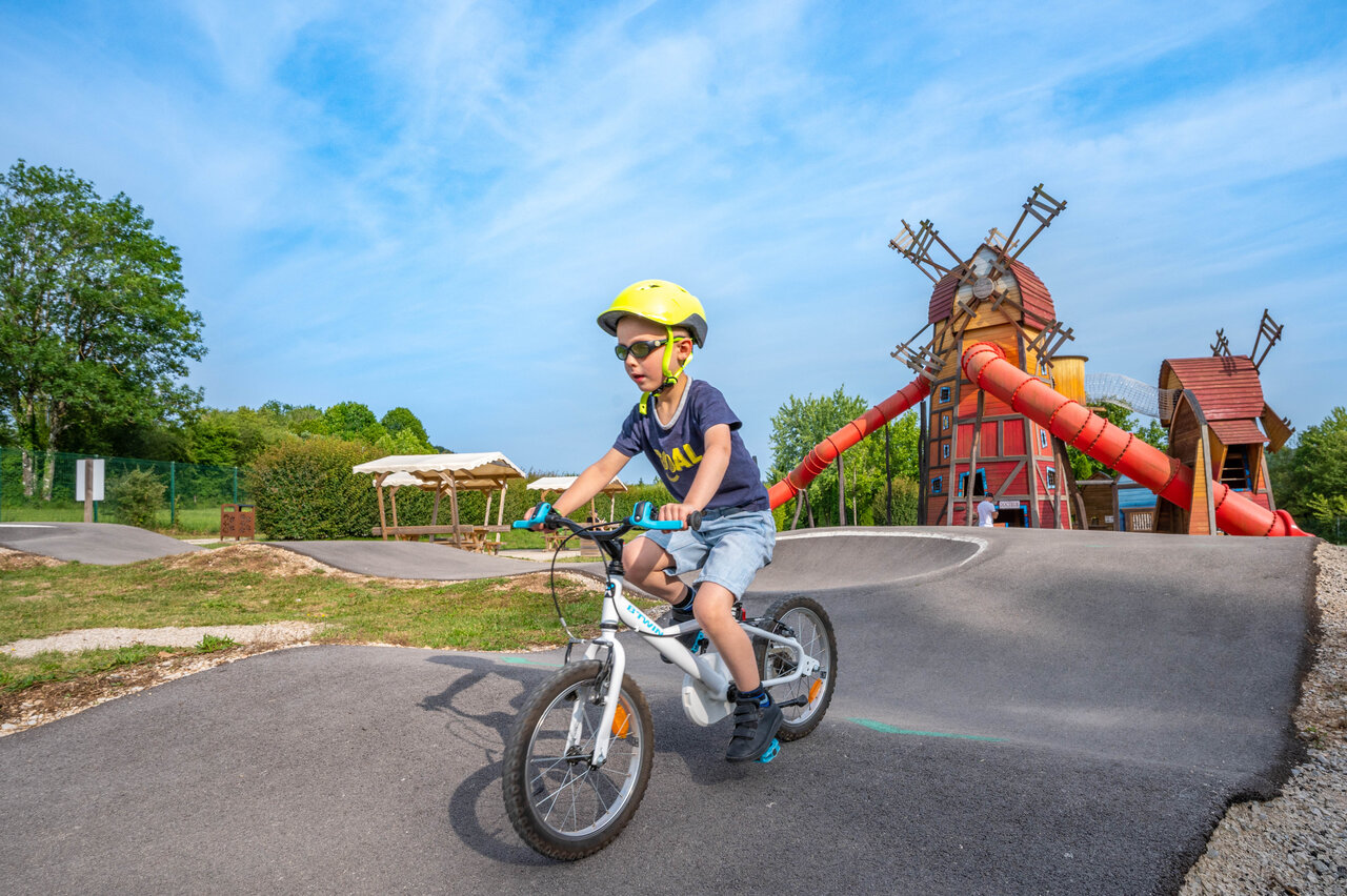 Enfant � v�lo sur un pump track avec aire de jeux moulin au camping CAPFUN Pergola � Marigny (39).