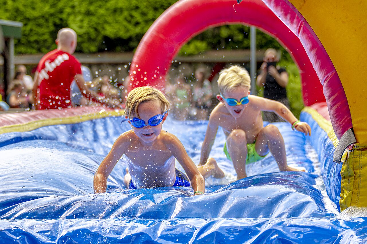 Enfants souriants jouant sur un toboggan aquatique gonflable au camping CAPFUN Ponderosa � Ulicoten.
