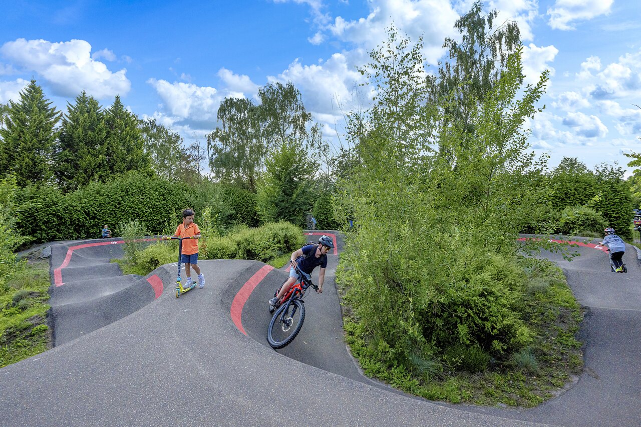 Piste de pump track avec cycliste et enfants en trottinette au camping CAPFUN Ponderosa � Ulicoten.