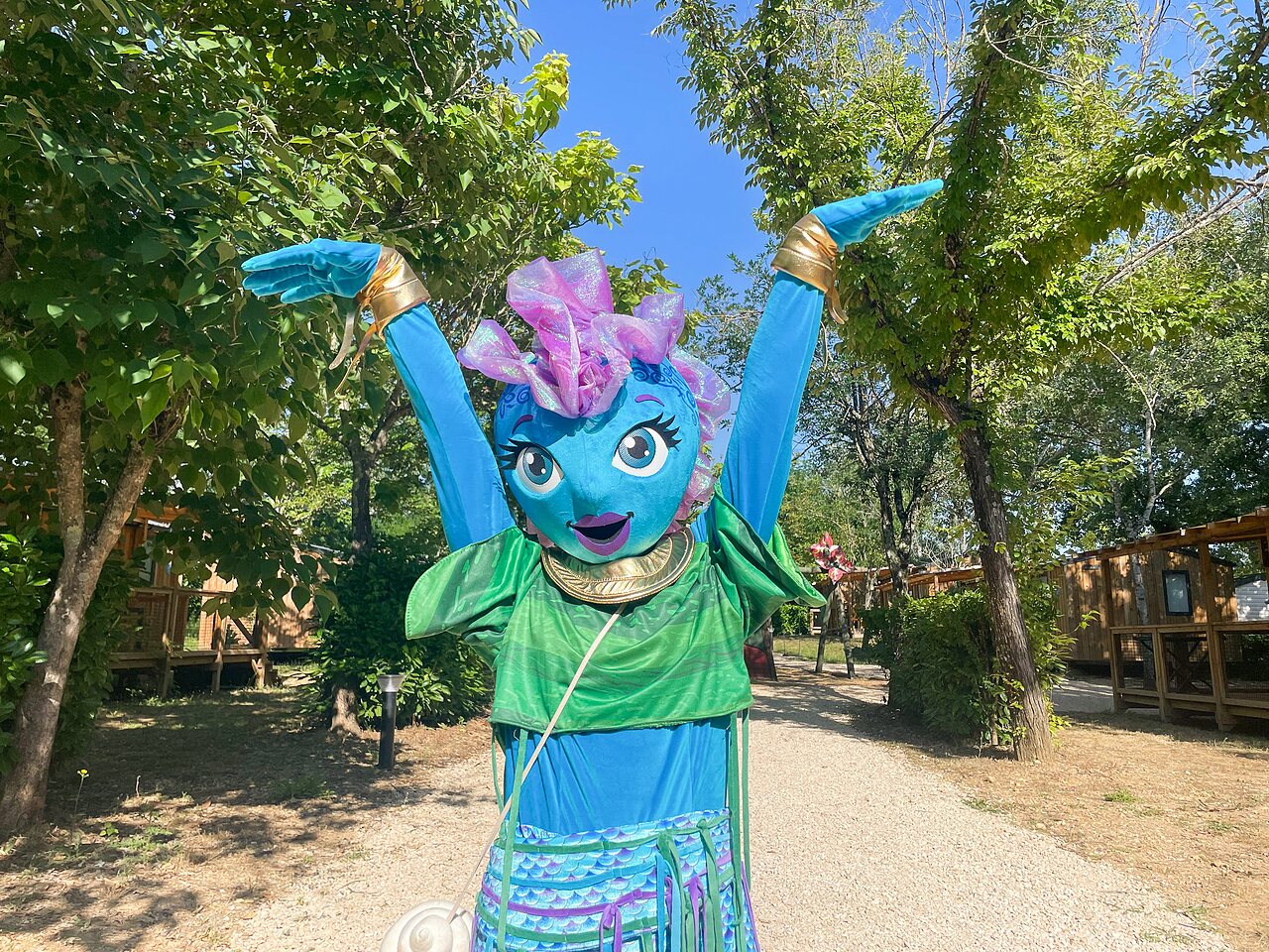 Smiling mascot with raised arms in front of Mobile homes at camping VAGUES OCEANES Pr�s de la Fontaine � Gouaix (77).