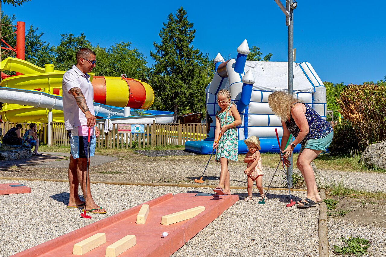 Famille jouant au mini-golf avec toboggans aquatiques et ch�teau gonflable au camping CAPFUN R�gni�re � VILLETTE D'ANTHON (38).