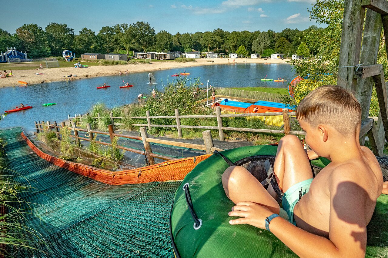 Enfant sur toboggan aquatique, lac et kayaks au camping CAPFUN het Stoetenslagh.
