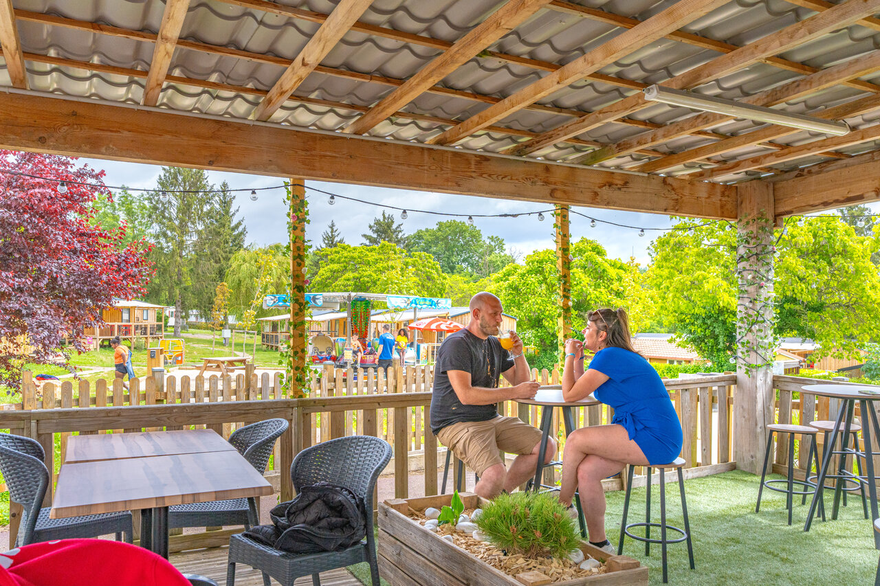 Lively bar terrace, couple and playground at CAPFUN Le Village Parisien campsite in VARREDDES (77).