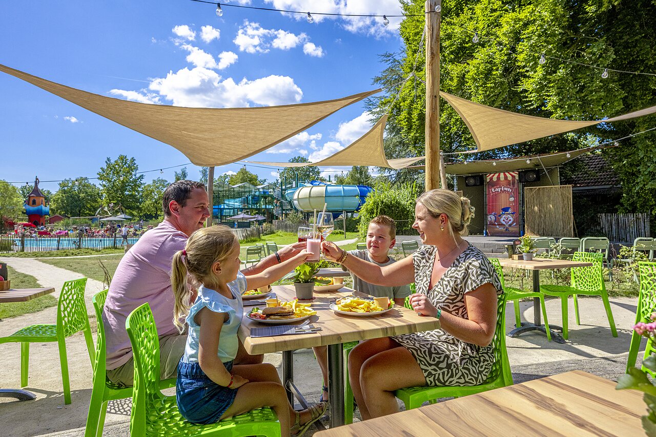 Famille d�jeunant en terrasse, piscine et toboggans au camping CAPFUN Vlinderloo � Enschede.